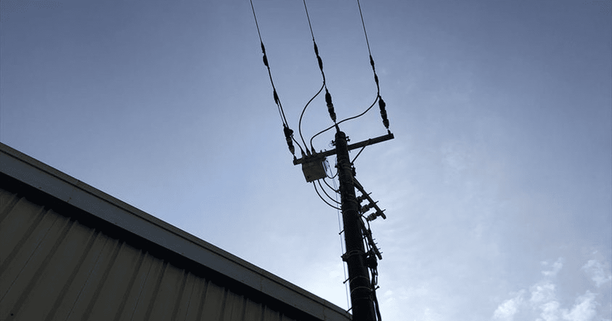屋根の脇に立つ電柱を逆光のシルエットで捉えた一枚