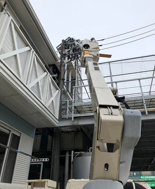 高所作業車のアームを伸ばして屋上設備の工事を行う様子