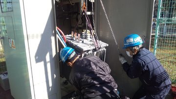 吊り具を使いトランス交換作業を行う作業員2名