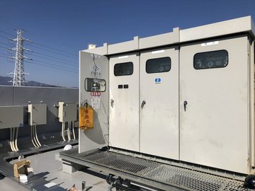屋上に設置されたキュービクルの全景と送電鉄塔の背景