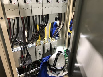 新しいキュービクルの中で、低圧の配線用遮断器に配線を接続する作業員