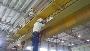 天井クレーンの桁で照明器具を取り付ける作業員