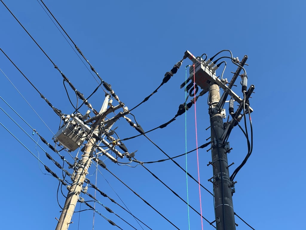 青空を背景にした電柱上部の開閉器と碍子、配線