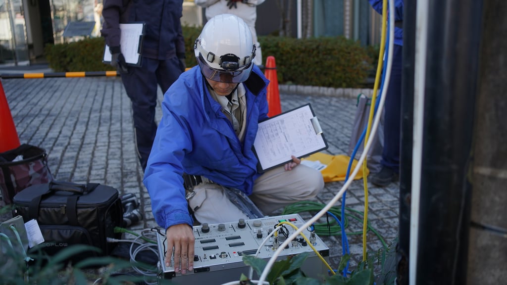 ヘルメット姿の作業員が屋外で点検記録を手に測定器を操作している様子