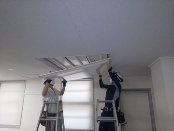 脚立に乗りオフィス天井の照明器具を取り付ける作業員2名