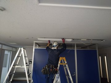 脚立に乗りオフィスの天井照明を交換する恒電社の電気工事士