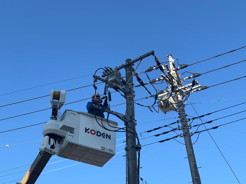青空の下、電柱上で作業員が開閉器の配線作業を行う様子