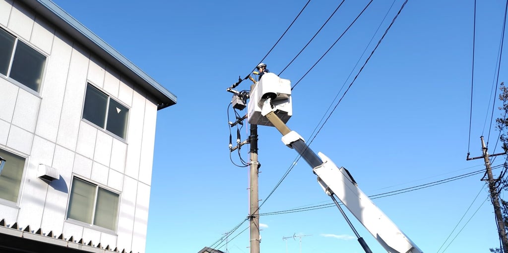 高所作業車のバケットに乗り電柱上で配線作業を行う恒電社の電気工事士