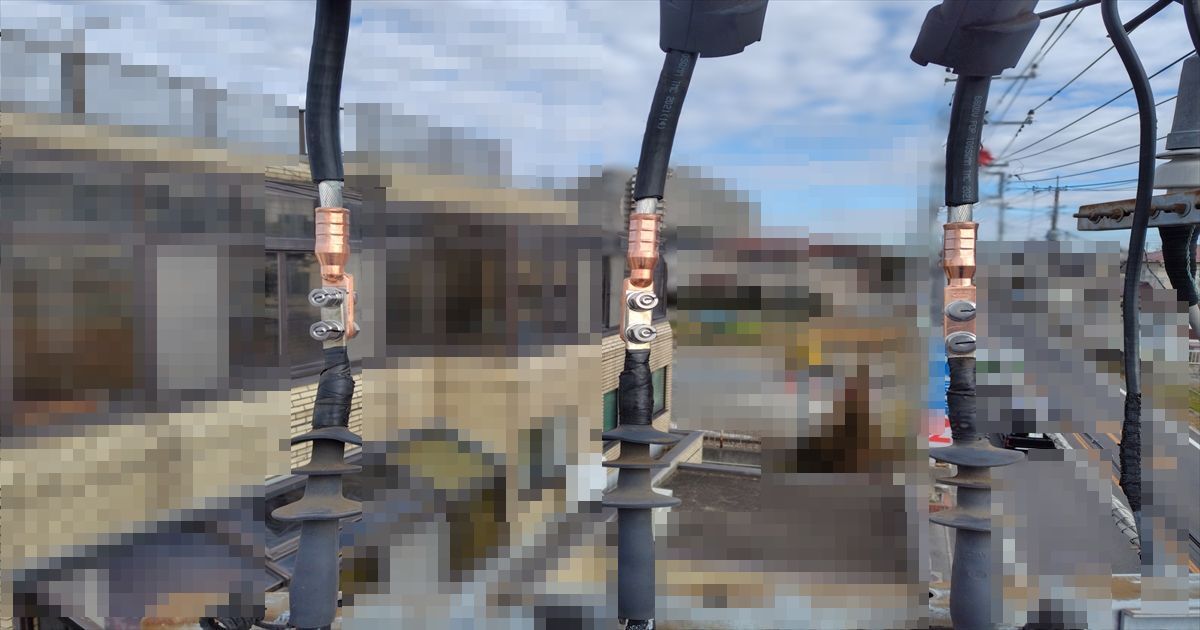 住宅街を背景に高圧ケーブルの端末処理3本が並ぶクローズアップ
