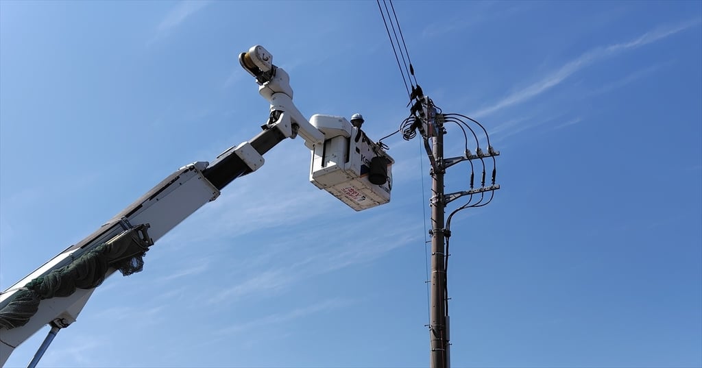 電柱脇でバケットを上げて作業する高所作業車
