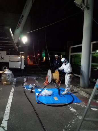 夜間、駐車場で新しい引込ケーブルをドラムから繰り出す作業の様子