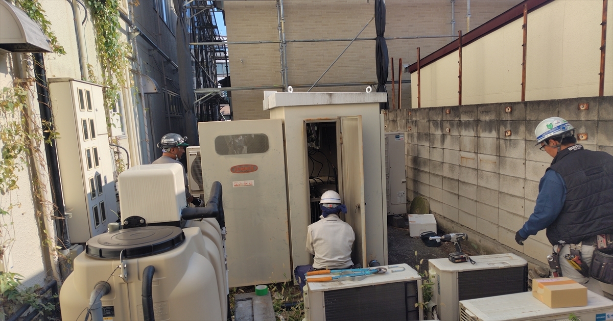 ビル裏の屋外キュービクルで作業する恒電社の電気工事士3名