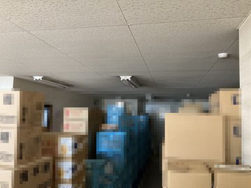 交換前：段ボールが積まれた保管スペースの天井照明